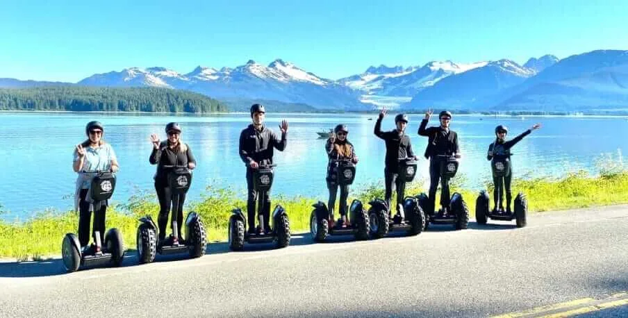segway_excursion Group on Segways waving by an Alaskan lake with snow-capped mountains in the background.